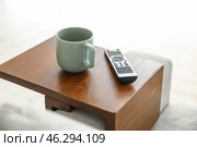 Cup of tea with remote control on armrest table in room. Стоковое фото, фотограф Pixel_shot / Фотобанк Лори