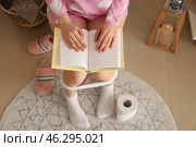 Young woman reading book while sitting on toilet bowl in restroom. Стоковое фото, фотограф Pixel_shot / Фотобанк Лори