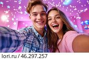 A happy young couple takes a selfie against the backdrop of bright garlands and sparkling snowflakes, conveying an atmosphere of joy, coziness and festive mood. Стоковое AI-изображение, AI-художник ArtVladZ / Фотобанк Лори