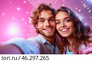 A happy young couple takes a selfie against the backdrop of bright garlands and sparkling snowflakes, conveying an atmosphere of joy, coziness and festive mood. Стоковое AI-изображение, AI-художник ArtVladZ / Фотобанк Лори
