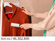 Woman cleaning sweater with lint roller on color background. Стоковое фото, фотограф Pixel_shot / Фотобанк Лори