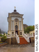 Chapel of the Nativity of Christ, located in the Laspi tract, Crimea. This is a small Orthodox chapel with classical architecture: a light facade, four columns at the entrance, a semicircular dome with a cross on top. Above the entrance is an image of Jesus Christ, and below it is a golden cross. A staircase with terracotta steps, framed by white railings with decorative balls, leads to the entrance. The open door of the chapel symbolically invites to prayer and spiritual reflection. (2021 год). Редакционное фото, фотограф Анна Кривицкая / Фотобанк Лори