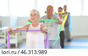Elderly woman kneeling performs exercises with wide elastic band during Pilates workout. Стоковое видео, видеограф Яков Филимонов / Фотобанк Лори