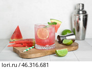 Board with glass of tasty watermelon cocktail, shaker, jigger and lime on white tile table. Стоковое фото, фотограф Pixel_shot / Фотобанк Лори