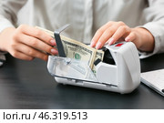 Female accountant putting money into currency counting machine on dark table. Стоковое фото, фотограф Pixel_shot / Фотобанк Лори
