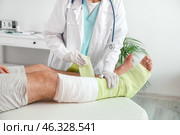 Doctor applying bandage on broken leg of young man in clinic. Стоковое фото, фотограф Pixel_shot / Фотобанк Лори