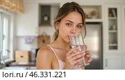 Beautiful young female enjoying clean water in bright kitchen, holding transparent glass, hydration and healthy, fresh look, morning wellness, relaxed pose, staying refreshed, home atmosphere. Стоковое AI-изображение, AI-художник Павел Муравьев / Фотобанк Лори
