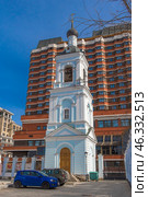 Contrast between the historical and modern architecture of Moscow. In the foreground is the bell tower of an ancient church, painted in blue and white, topped with an onion-shaped dome with a cross. Church bells hang in the opening of the tower.In the background rises the President Hotel, a monumental Soviet building with its characteristic beige brick cladding, many windows and cascading structure.This image perfectly demonstrates the coexistence of religious heritage and Soviet modernism, typical of Moscow. Стоковое фото, фотограф Анна Кривицкая / Фотобанк Лори