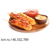 Wooden plate with tasty corn dogs and bowls of different sauces on white background. Стоковое фото, фотограф Pixel_shot / Фотобанк Лори