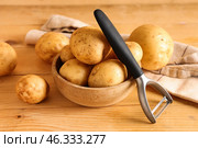 Bowl with raw potatoes and peeler on wooden background. Стоковое фото, фотограф Pixel_shot / Фотобанк Лори