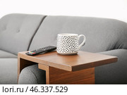 Cup of tea with remote control on armrest table in room. Стоковое фото, фотограф Pixel_shot / Фотобанк Лори