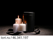 Mortuary urn, burning candles and black ribbon on table against dark background. Стоковое фото, фотограф Pixel_shot / Фотобанк Лори