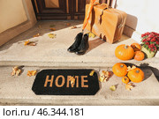Doormat with shoes, suitcase, umbrella and pumpkins near entrance of house on autumn day. Стоковое фото, фотограф Pixel_shot / Фотобанк Лори