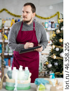 Middle-aged man restocking using tablet in store with New Year decoration. Стоковое фото, фотограф Яков Филимонов / Фотобанк Лори
