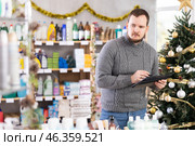 Bearded man seller restock of goods using tablet in store decorated for New Year holiday. Стоковое фото, фотограф Яков Филимонов / Фотобанк Лори