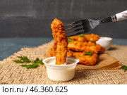 Dipping of tasty nugget in sauce on dark table, closeup. Стоковое фото, фотограф Pixel_shot / Фотобанк Лори