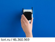 Woman plugging black WiFi repeater in electric socket on blue wall. Стоковое фото, фотограф Pixel_shot / Фотобанк Лори