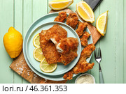 Plates of tasty fried codfish with lemon on green wooden background. Стоковое фото, фотограф Pixel_shot / Фотобанк Лори