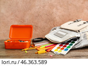 Grey school backpack with different stationery and lunchbox on wooden table near beige grunge wall. Стоковое фото, фотограф Pixel_shot / Фотобанк Лори