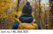 Adventurer among an Autumn Landscape. Back View of Young Woman Wearing Knitted Hat, Jacket, Backpack in Forest Woods Nature. Beauty and Adventure. Vibrant colorful fall scenery. Travel hike. Journey. Стоковое AI-видео, аниматор Марина Демидюк / Фотобанк Лори