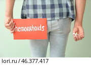 Young man holding paper with text HEMORRHOIDS and suppository on color background. Стоковое фото, фотограф Pixel_shot / Фотобанк Лори