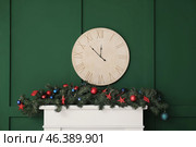 Mantelpiece with Christmas decor and clock on green wall in room. Стоковое фото, фотограф Pixel_shot / Фотобанк Лори