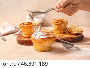 Woman adding sugar powder onto tasty cruffins on beige background. Стоковое фото, фотограф Pixel_shot / Фотобанк Лори