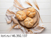 Board with delicious kaiser rolls and wheat ears on white wooden background. Стоковое фото, фотограф Pixel_shot / Фотобанк Лори
