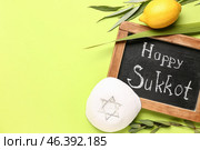 Four species (lulav, hadas, arava, etrog), kippah and chalkboard with text HAPPY SUKKOT on green background. Стоковое фото, фотограф Pixel_shot / Фотобанк Лори