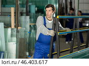 Man glazer employee in blue overall works in glass processing shop. Стоковое фото, фотограф Яков Филимонов / Фотобанк Лори