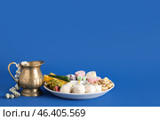 Diya lamp with jug, beads and plate of different treats on blue background. Divaly celebration. Стоковое фото, фотограф Pixel_shot / Фотобанк Лори