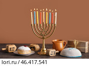 Menorah with doughnut, gift, Jewish hat and dreidels for Hannukah celebration on table near brown wall. Стоковое фото, фотограф Pixel_shot / Фотобанк Лори
