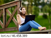 Cheerful woman in wireless headphones makes telework with laptop outdoors. Стоковое фото, фотограф Владимир Григорьев / Фотобанк Лори