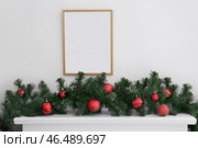 Пустая рамка и новогодние ветки с шарами на каминной полке в гостиной. Стоковое фото, фотограф Pixel_shot / Фотобанк Лори