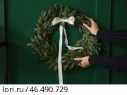 Женщина вешает рождественский венок на зеленую стену дома. Стоковое фото, фотограф Pixel_shot / Фотобанк Лори