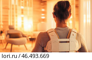 Woman wearing posture corrector brace at home standing in living room. Стоковое AI-изображение, AI-художник Юрий Поздников / Фотобанк Лори