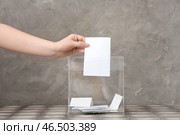 Женщина голосует у избирательной урны на столе на фоне серого фона. Стоковое фото, фотограф Pixel_shot / Фотобанк Лори