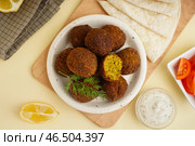 Тарелка с вкусными фалафельными шариками, помидорами, соусом и питой на бежевом фоне. Стоковое фото, фотограф Pixel_shot / Фотобанк Лори