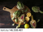 Деревянная доска с сырыми артишоками и лимонами на столе. Стоковое фото, фотограф Pixel_shot / Фотобанк Лори