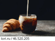 Наливание молока в стакан с вкусным кофе со льдом и круассаном на столе. Стоковое фото, фотограф Pixel_shot / Фотобанк Лори