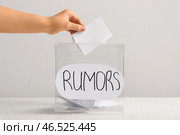 Женщина кладет бумагу в коробку с надписью «СЛУХИ» на столе на светлом фоне. Концепция сплетен. Стоковое фото, фотограф Pixel_shot / Фотобанк Лори