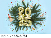 Цифра 2025 из фольгированных шаров с рождественскими украшениями, еловыми ветвями и конфетти на синем фоне. Стоковое фото, фотограф Pixel_shot / Фотобанк Лори