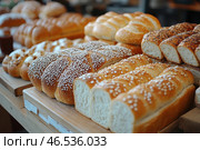 An assortment of freshly baked breads, neatly laid out on wooden trays in a bakery or market. The breads come in a variety of shapes and textures – braided loaves, loaves sprinkled with sugar, sesame and seeds. Their golden crusts and soft crumbs convey the feeling of freshness and aroma of home baking.Soft lighting highlights the texture of the bread, creating a warm, cozy atmosphere. The different types of bread symbolize baking traditions and gastronomic pleasure. Стоковое AI-изображение, AI-художник Анна Кривицкая / Фотобанк Лори