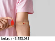 Молодой донор крови с наклеенным медицинским пластырем и бумажной каплей на светлом фоне, крупным планом. Стоковое фото, фотограф Pixel_shot / Фотобанк Лори
