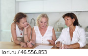 Three women help each other sort out financial documents in the kitchen of a home. Стоковое видео, видеограф Яков Филимонов / Фотобанк Лори