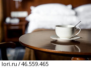 A white cup of hot tea or coffee on a wooden table in the interior of a hotel room. The concept of drinks and comfortable hotel accommodation. Стоковое фото, фотограф Photojuli / Фотобанк Лори