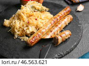 Сланцевая тарелка с вкусной квашеной капустой и жареными сосисками на темном фоне, крупным планом. Стоковое фото, фотограф Pixel_shot / Фотобанк Лори