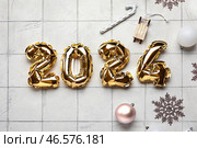 Фигура 2024 из фольгированных шариков с рождественскими шариками, снежинками и леденцами на белом плиточном фоне. Стоковое фото, фотограф Pixel_shot / Фотобанк Лори