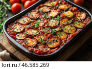 A delicious oven-baked dish. This is a vegetable casserole with eggplant, tomato sauce and aromatic herbs. The eggplant slices are evenly distributed over the surface, lightly browned and covered with a thin layer of herbs and spices. The casserole is served in a ceramic dish, and fresh tomatoes, garlic and herbs are scattered around, creating a cozy, rustic atmosphere. Стоковое AI-изображение, AI-художник Анна Кривицкая / Фотобанк Лори