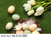 Гнездышко с расписными пасхальными яйцами, перьями и цветами на зеленом фоне. Стоковое фото, фотограф Pixel_shot / Фотобанк Лори